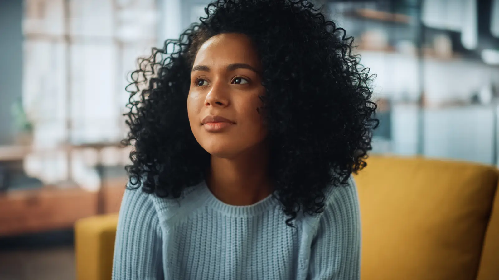 Latina woman wearing a sweater in a bright creative room gazing slightly to her right.